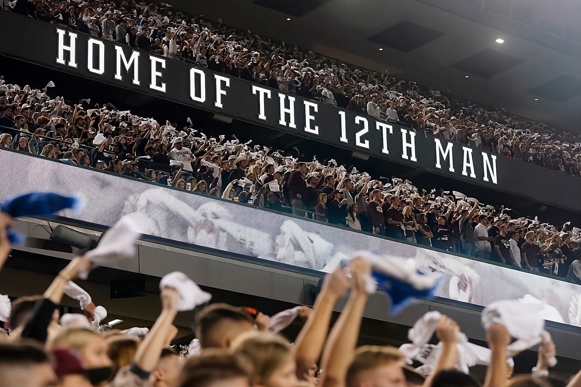 Texas A&M fans with a stadium sign that says "Home of the 12th Man."